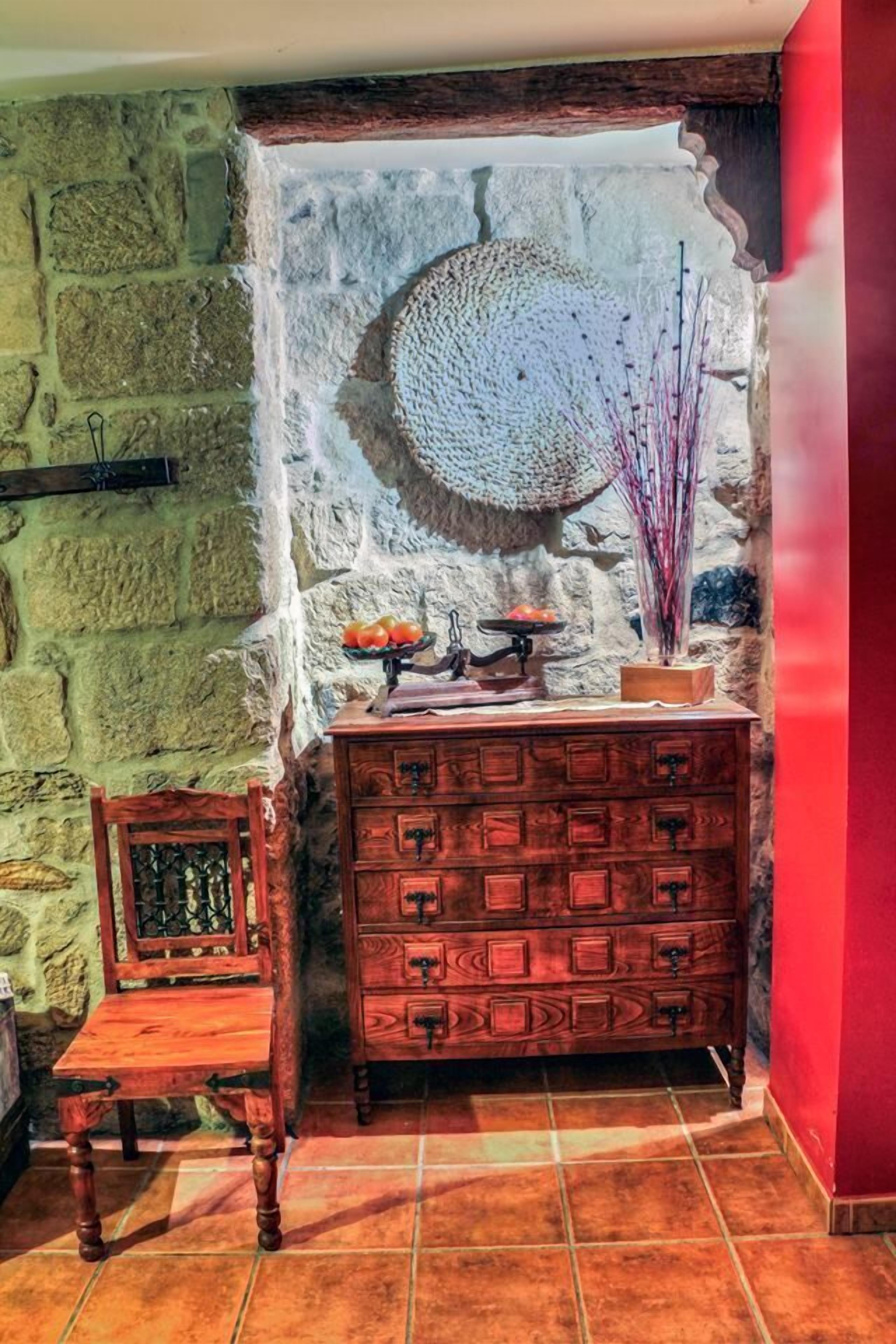Een rustieke kamer met een stenen muur, een houten dressoir, een stoel en een decoratieve wandversiering.