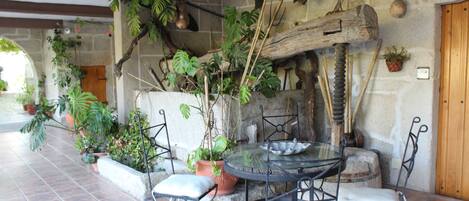En terrasse med et rundt glasbord, fire metalstole og forskellige krukker med planter.