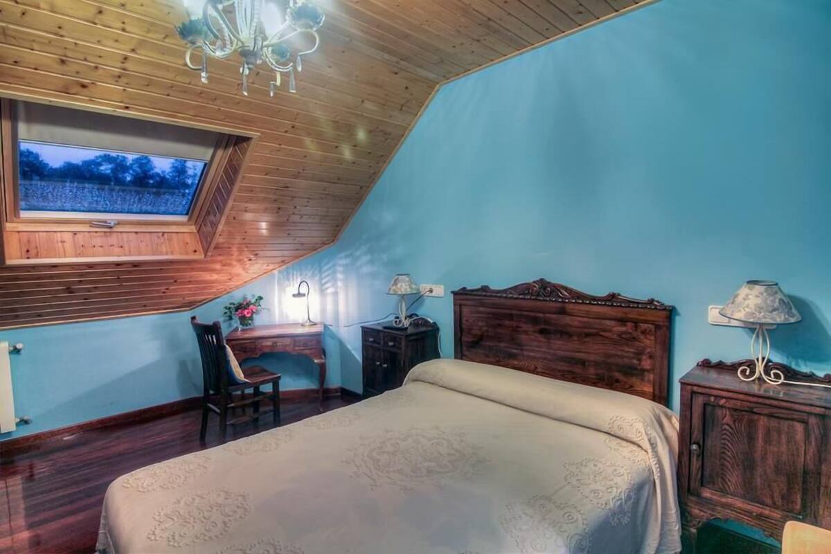 A bedroom with a sloped ceiling, a skylight, a wooden bed, a desk, and a chair.
