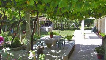 Un patio con una mesa y sillas de piedra, rodeado de plantas en macetas y una pérgola cubierta de hiedra.