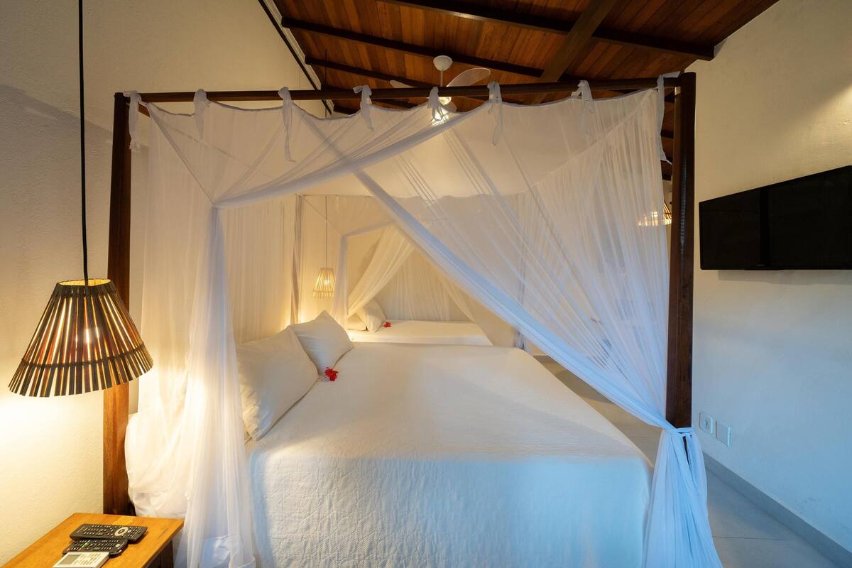 Uma cama com dossel, um abajur e um controle remoto sobre uma mesa de cabeceira de madeira.