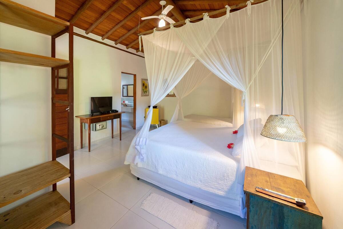 Quarto com cama de dossel, uma escrivaninha com computador e televisão.