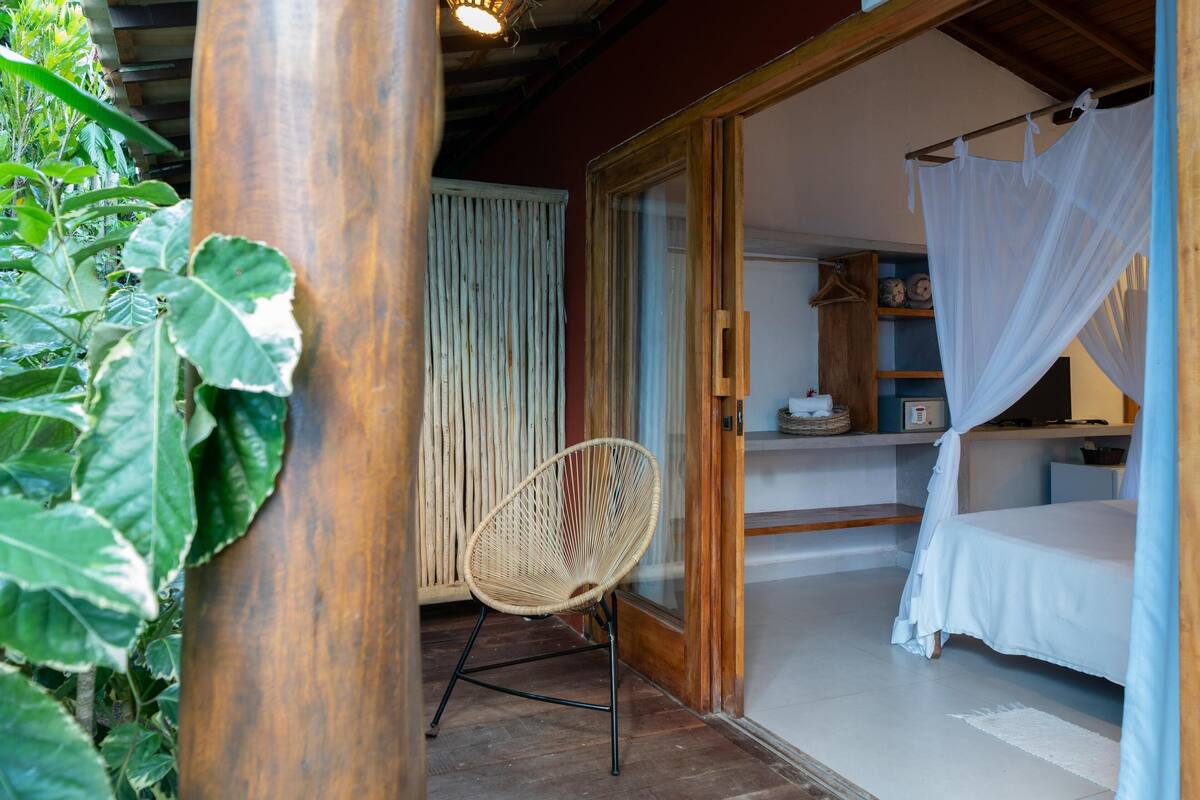Quarto com cama, cadeira e janela com cortinas.
