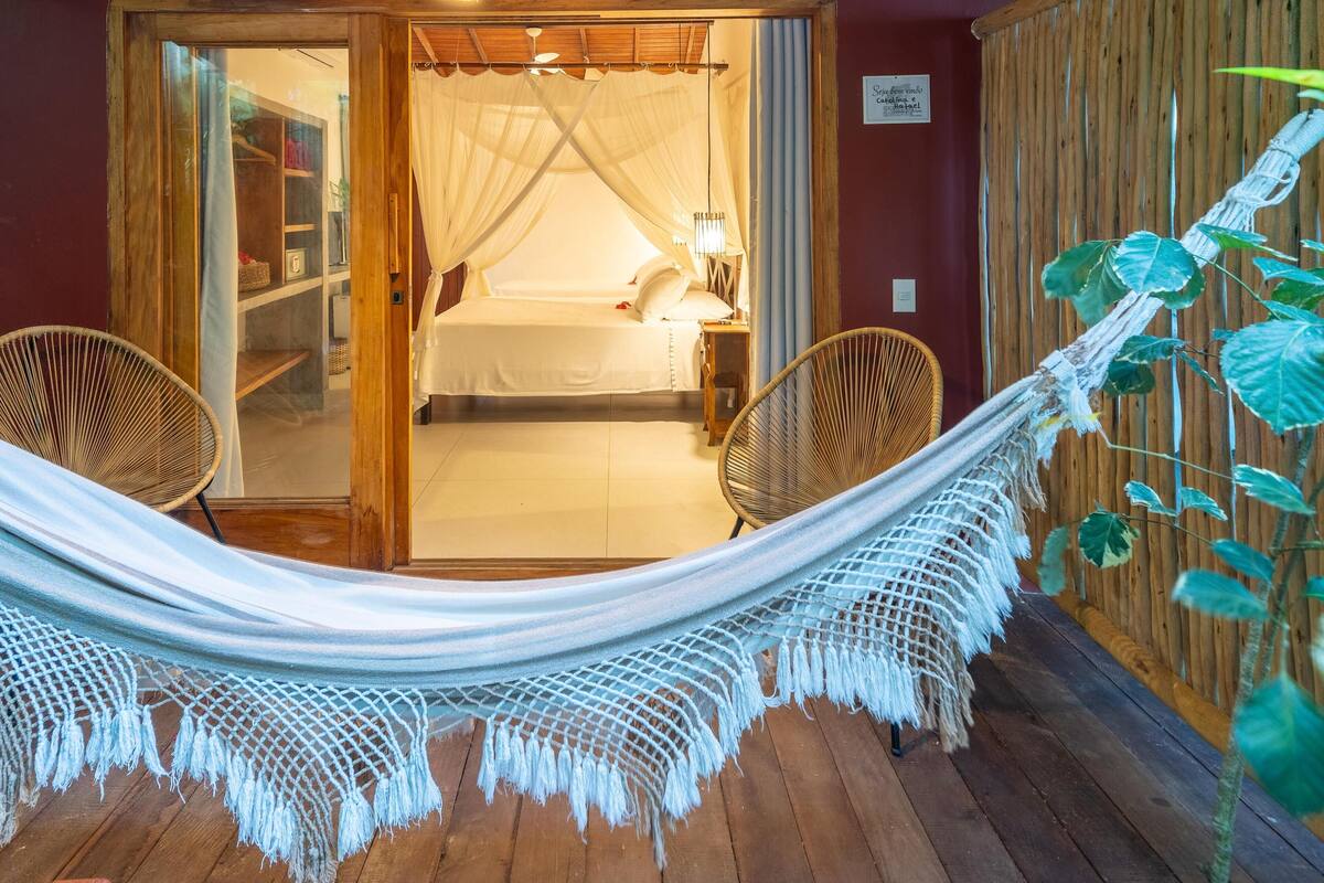 Quarto com cama, poltrona, rede e piso de madeira.