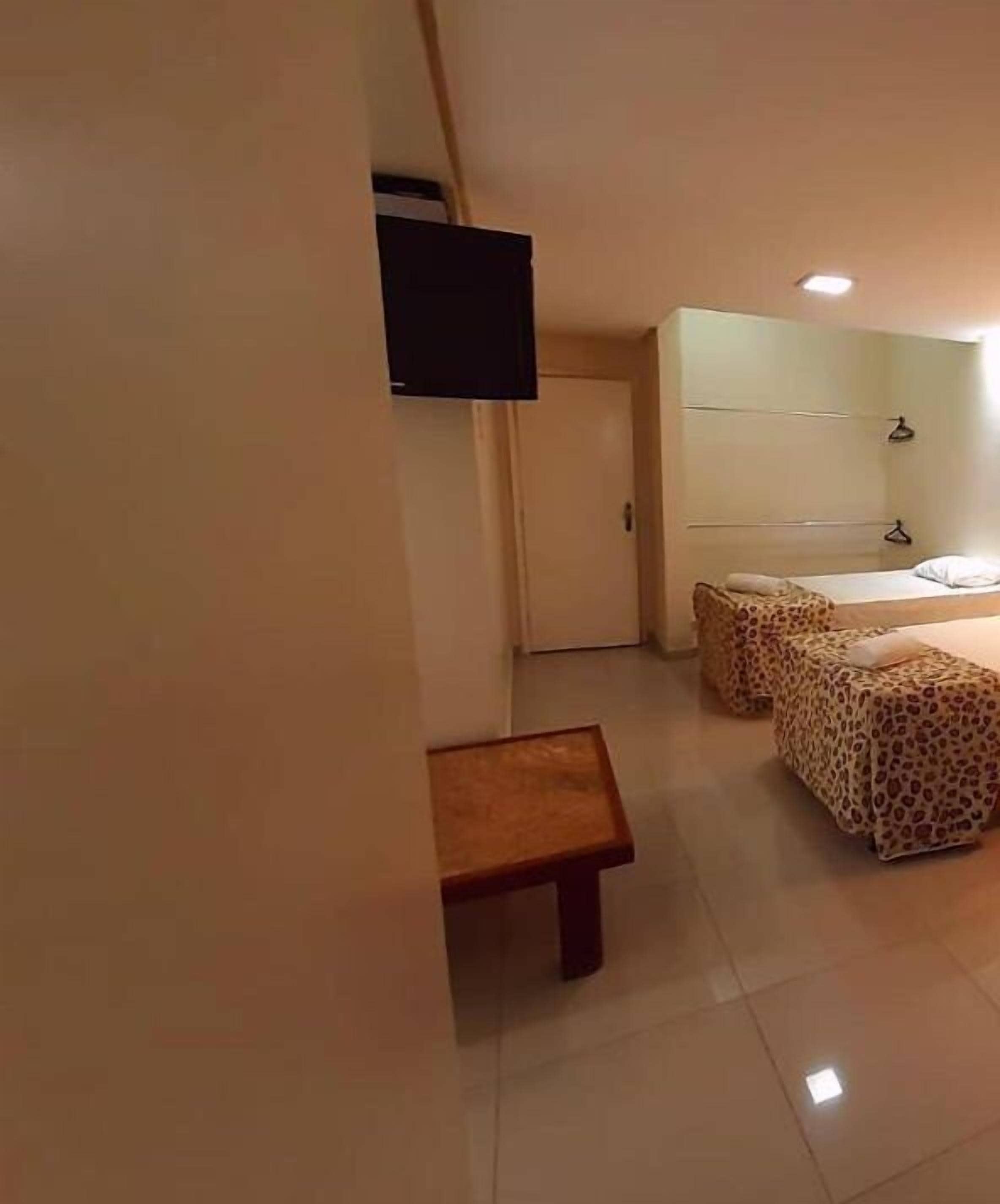 A hotel room with a bed, a small table, a wardrobe, and a television mounted on the wall.