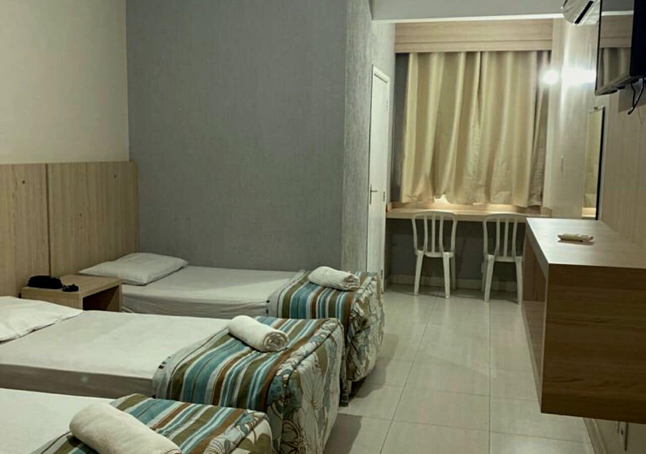 Habitación de hotel con dos camas individuales, un escritorio pequeño y una silla.