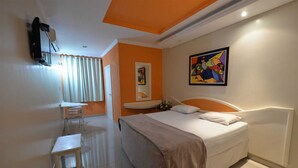 A hotel room with a bed, a desk, a chair, a mirror, and a painting on the wall. - Biss Inn (Goiania)