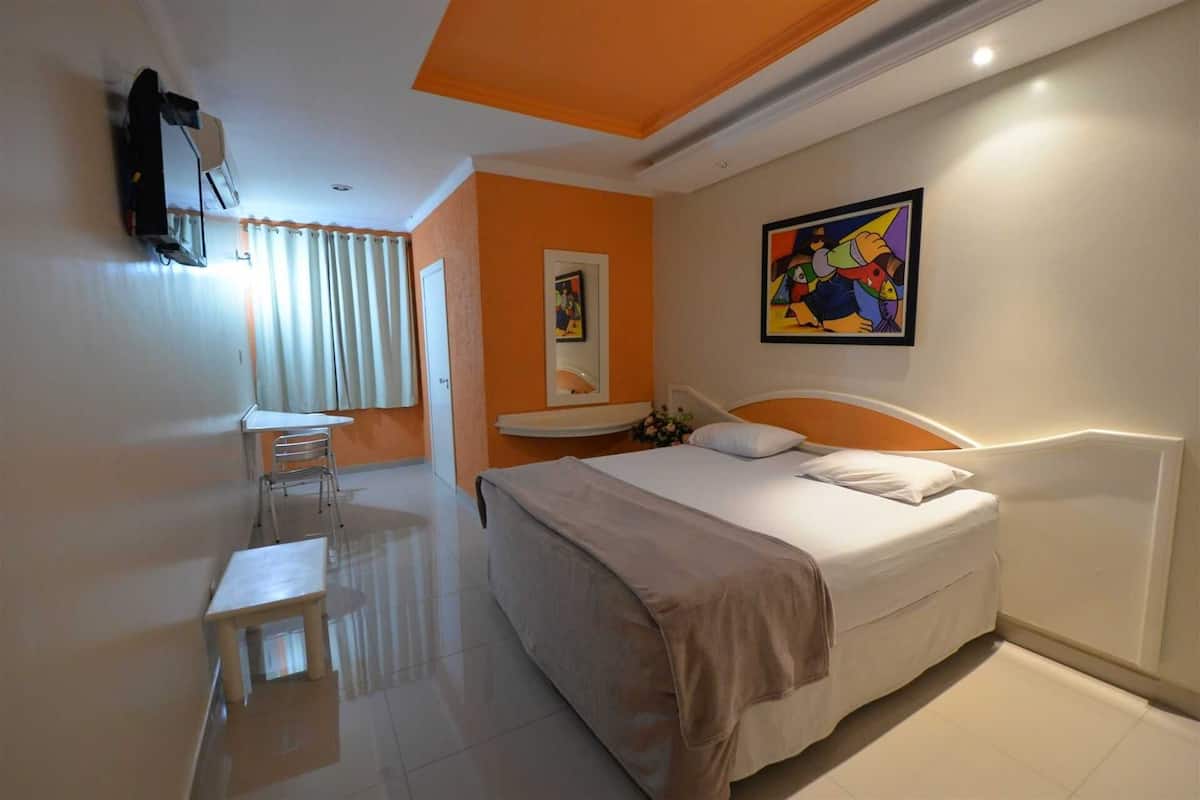 A hotel room with a bed, a desk, a chair, a mirror, and a painting on the wall.