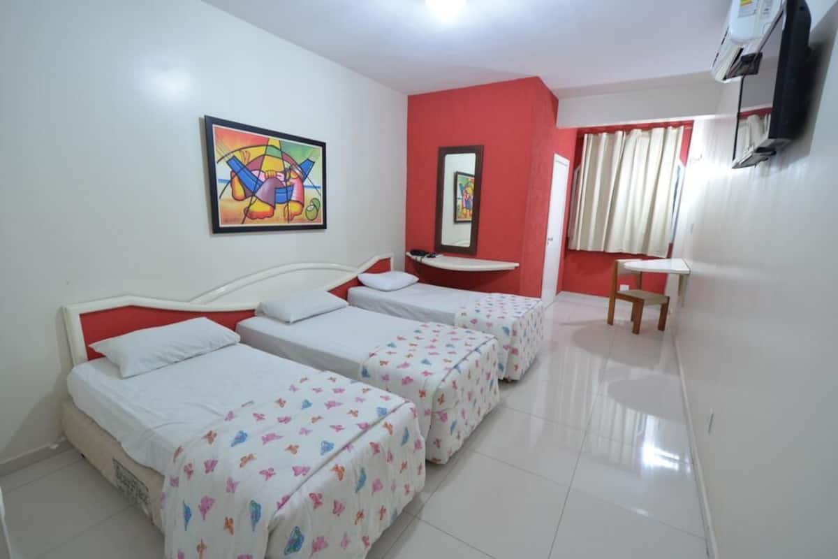 A hotel room with two beds, a small desk, a mirror, and a colorful painting on the wall.