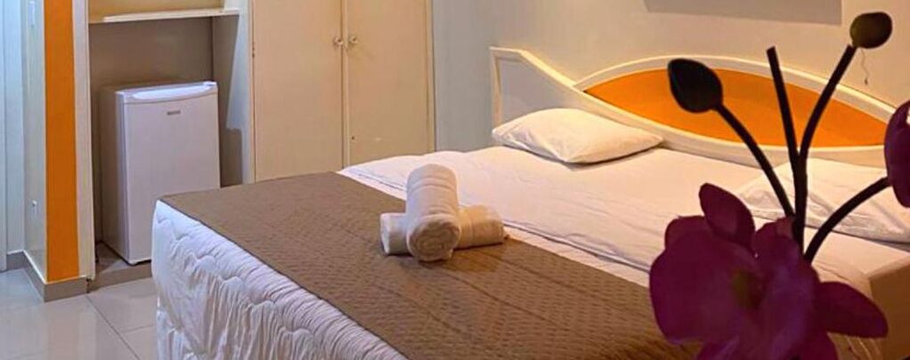 Ett hotellrum med en säng, ett litet vitt kylskåp och ett badrum med ett vitt skåp.