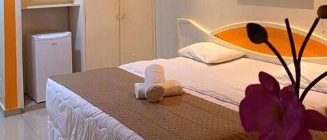 Ett hotellrum med en säng, ett litet vitt kylskåp och ett badrum med ett vitt skåp.
