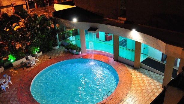 An indoor swimming pool with a tiled floor, surrounded by potted plants and chairs. - Biss Inn (Goiania)