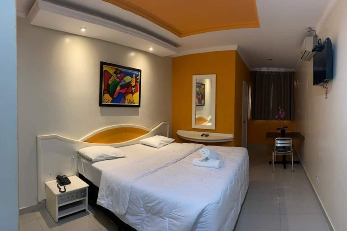 A hotel room with a bed, a nightstand, a mirror, a sink, and a chair.