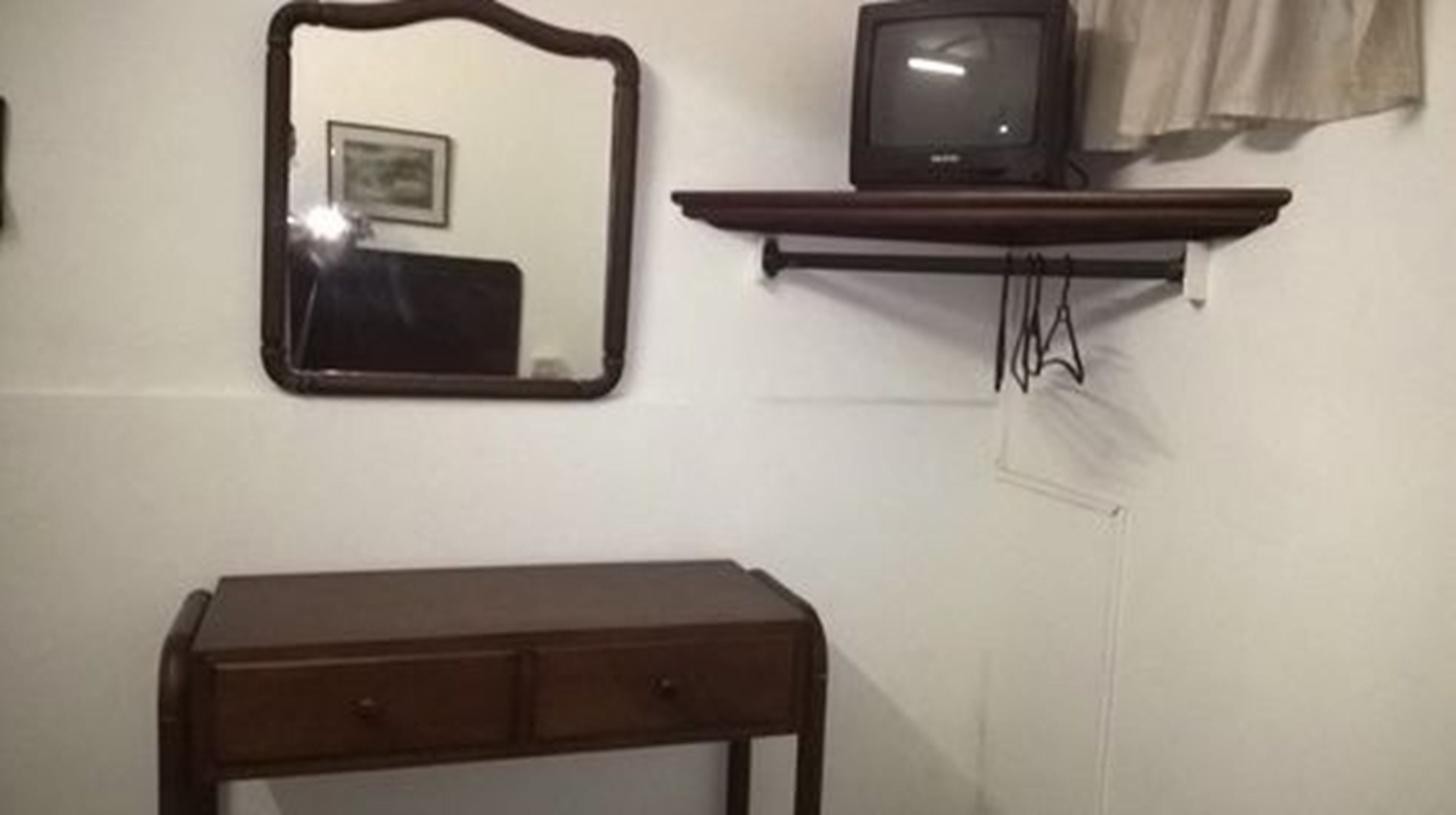 A room with a wooden dresser, a mirror, and a television on a stand.