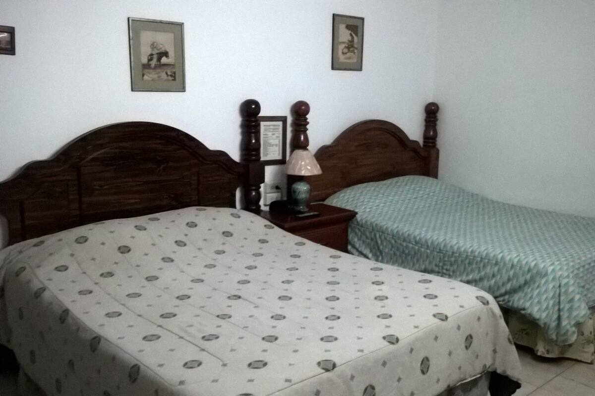 A bedroom with two beds, a nightstand with a lamp, and framed pictures on the wall.