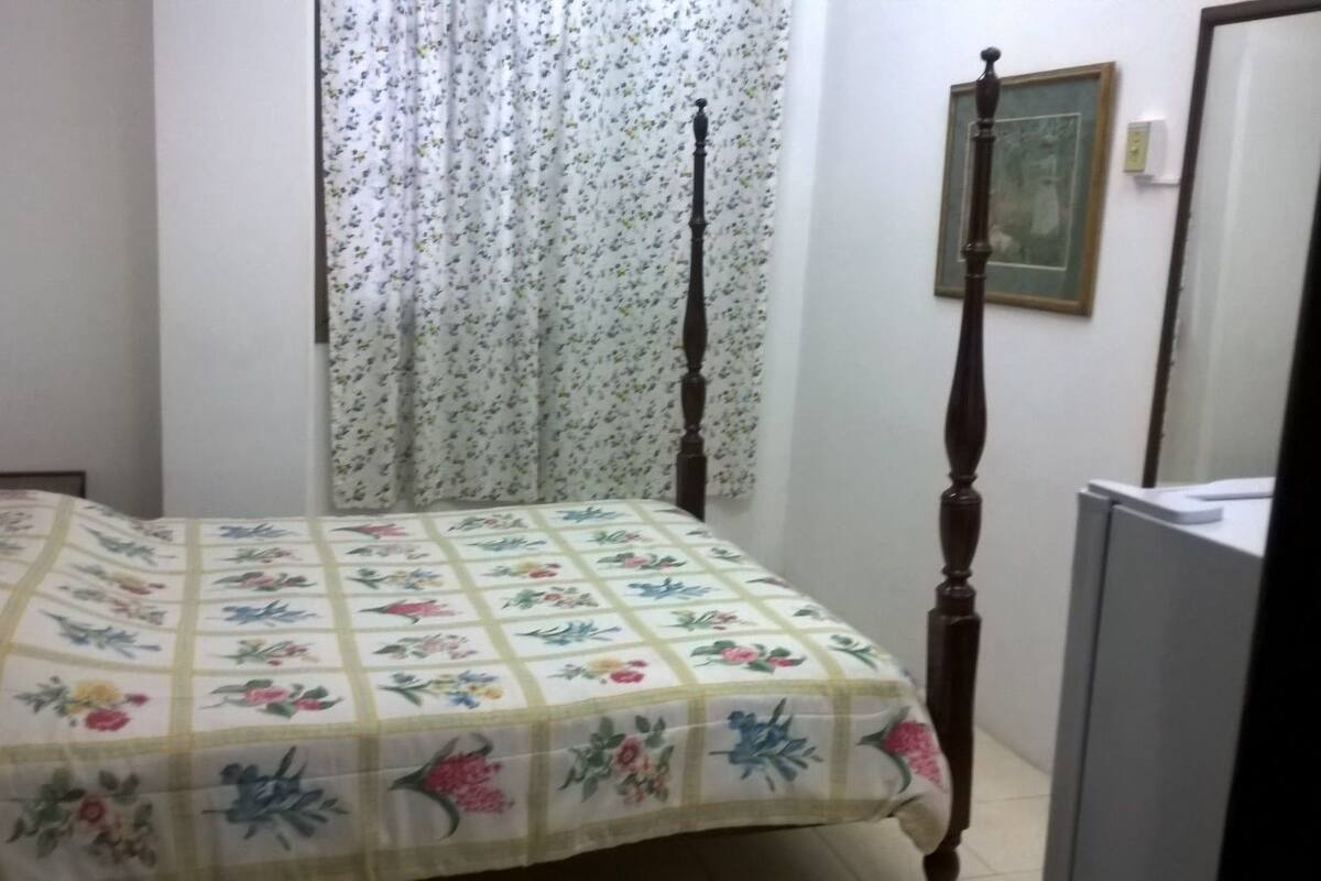 A bedroom with a bed, curtains, a painting, and a television.