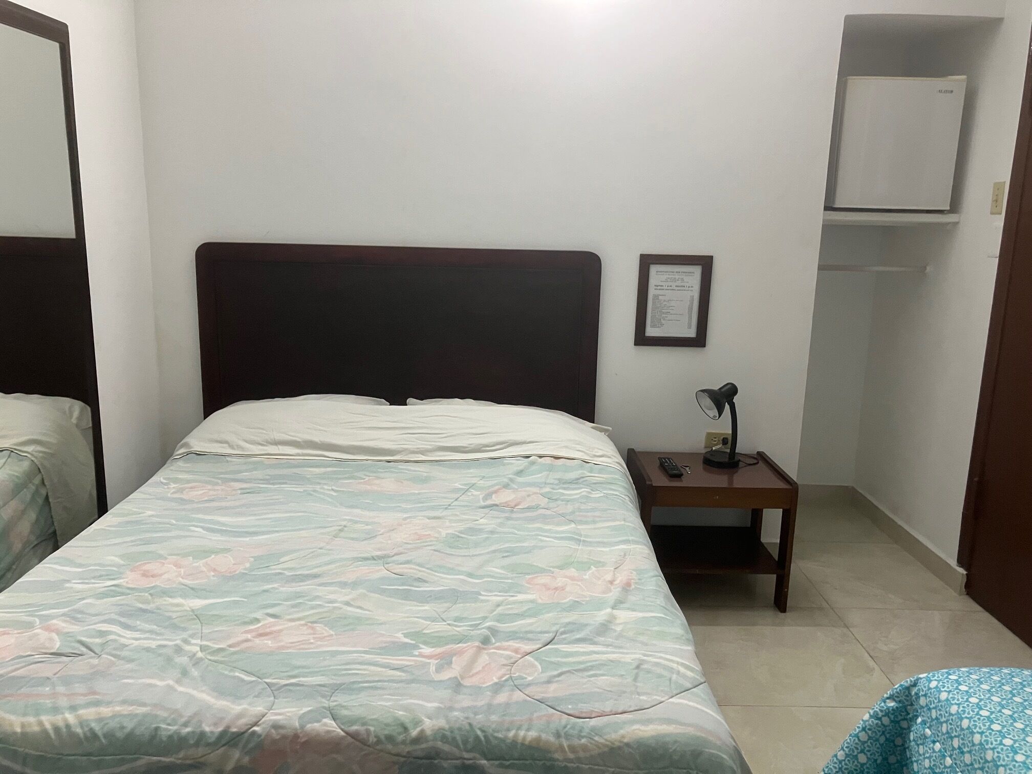 Une chambre à coucher comprenant un lit, une table de chevet, une lampe, un certificat encadré accroché au mur et une armoire.