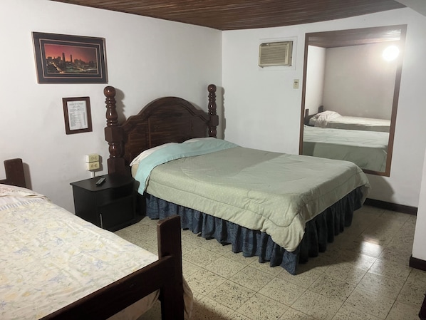 A bedroom with a wooden bed, a nightstand, a framed certificate, a cityscape picture, and a mirror reflecting the bed.