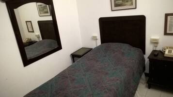 A bedroom with a bed, a nightstand, a bedside table, a mirror, and a wall-mounted telephone.