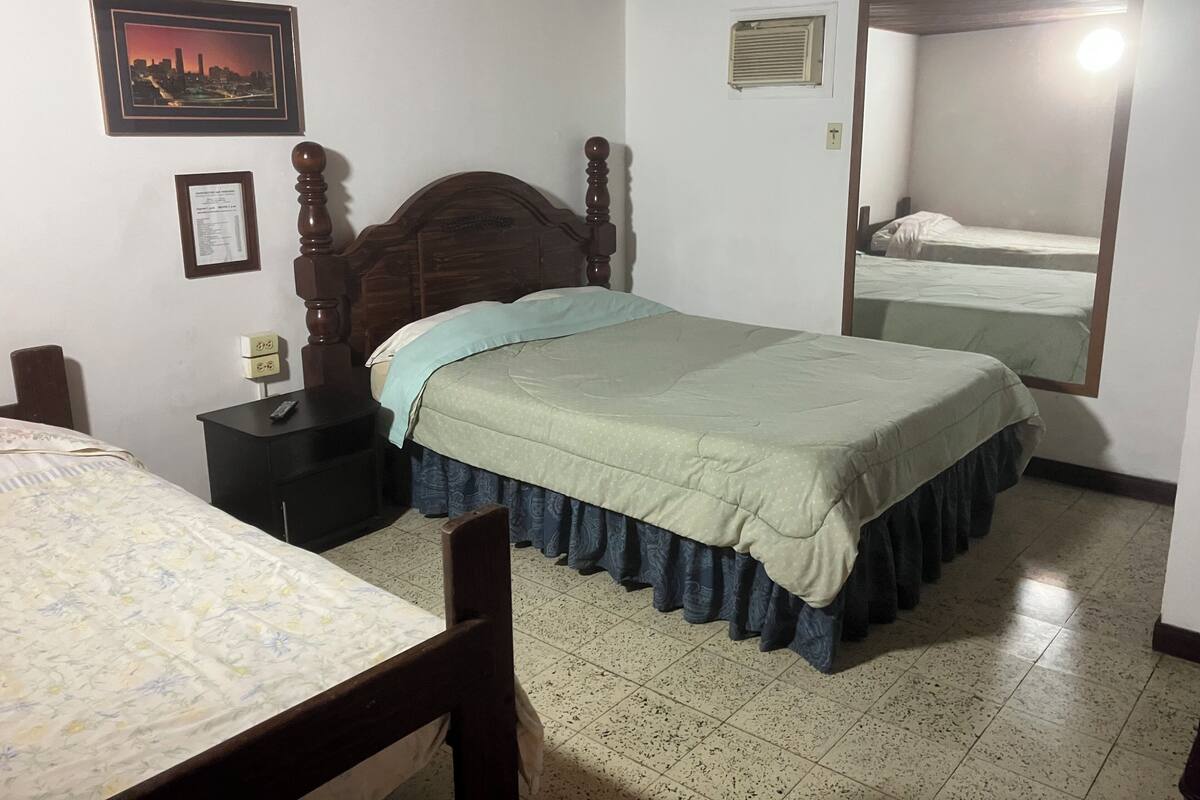 A bedroom with a wooden bed, a nightstand, a framed certificate, and a cityscape picture on the wall.