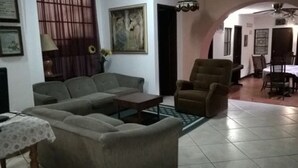 A living room with a sofa, armchair, and a small table. There is a painting on the wall and a door leading to another room. - Hostal San Fernando (Cali)