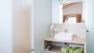 A modern bathroom with a glass shower enclosure, a white sink, and a mirror reflecting a window with curtains.