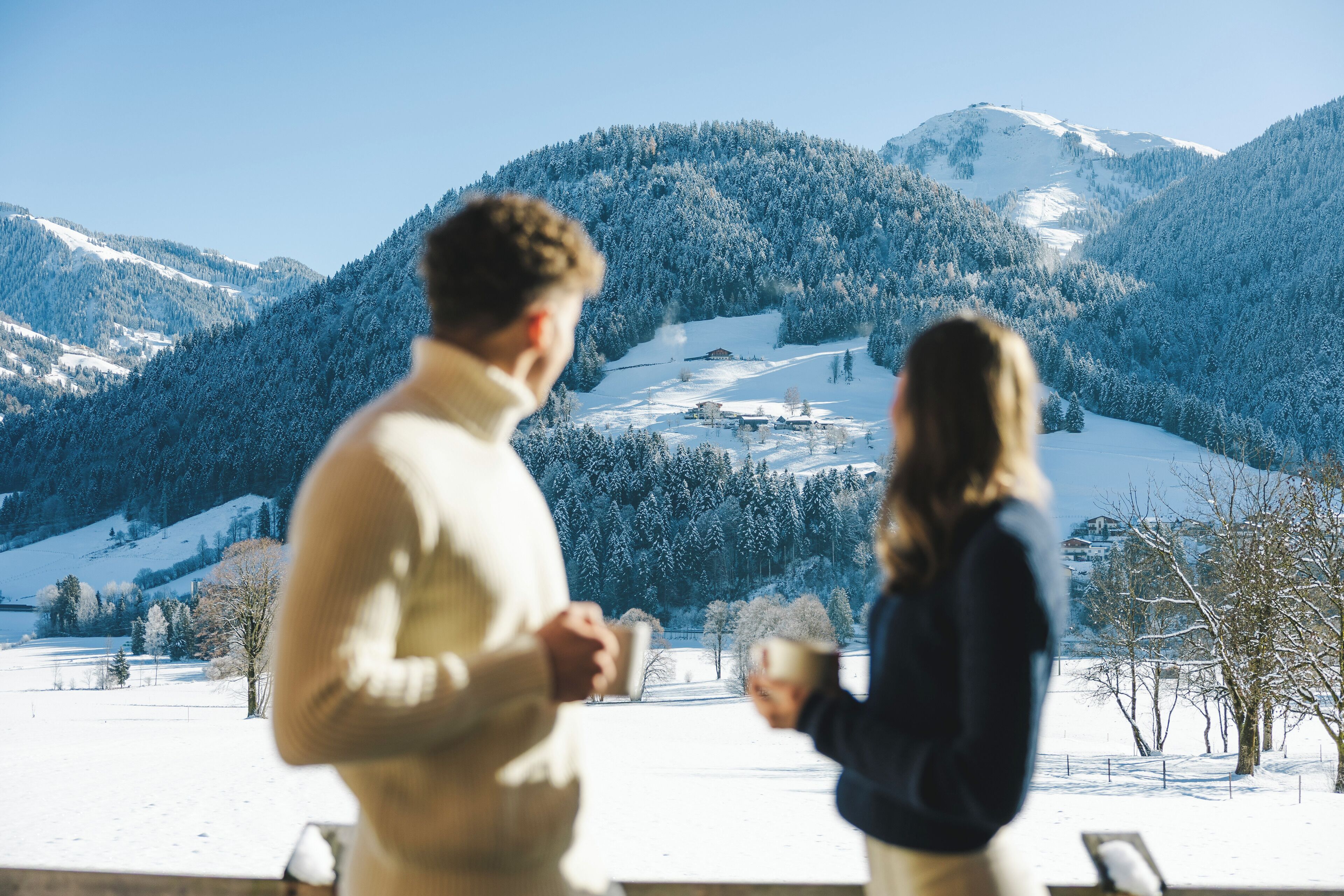 A couple standing by a window overlooking a snowy mountain landscape.