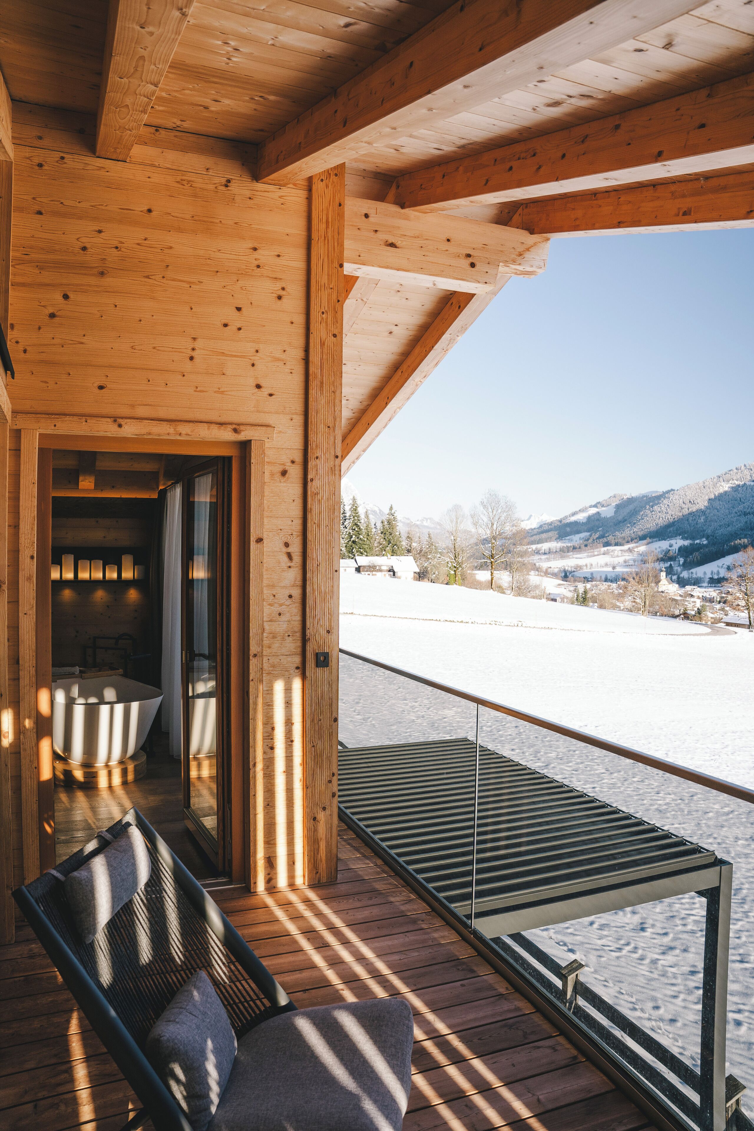Una terraza de madera con barandilla de vidrio que da a un paisaje nevado.