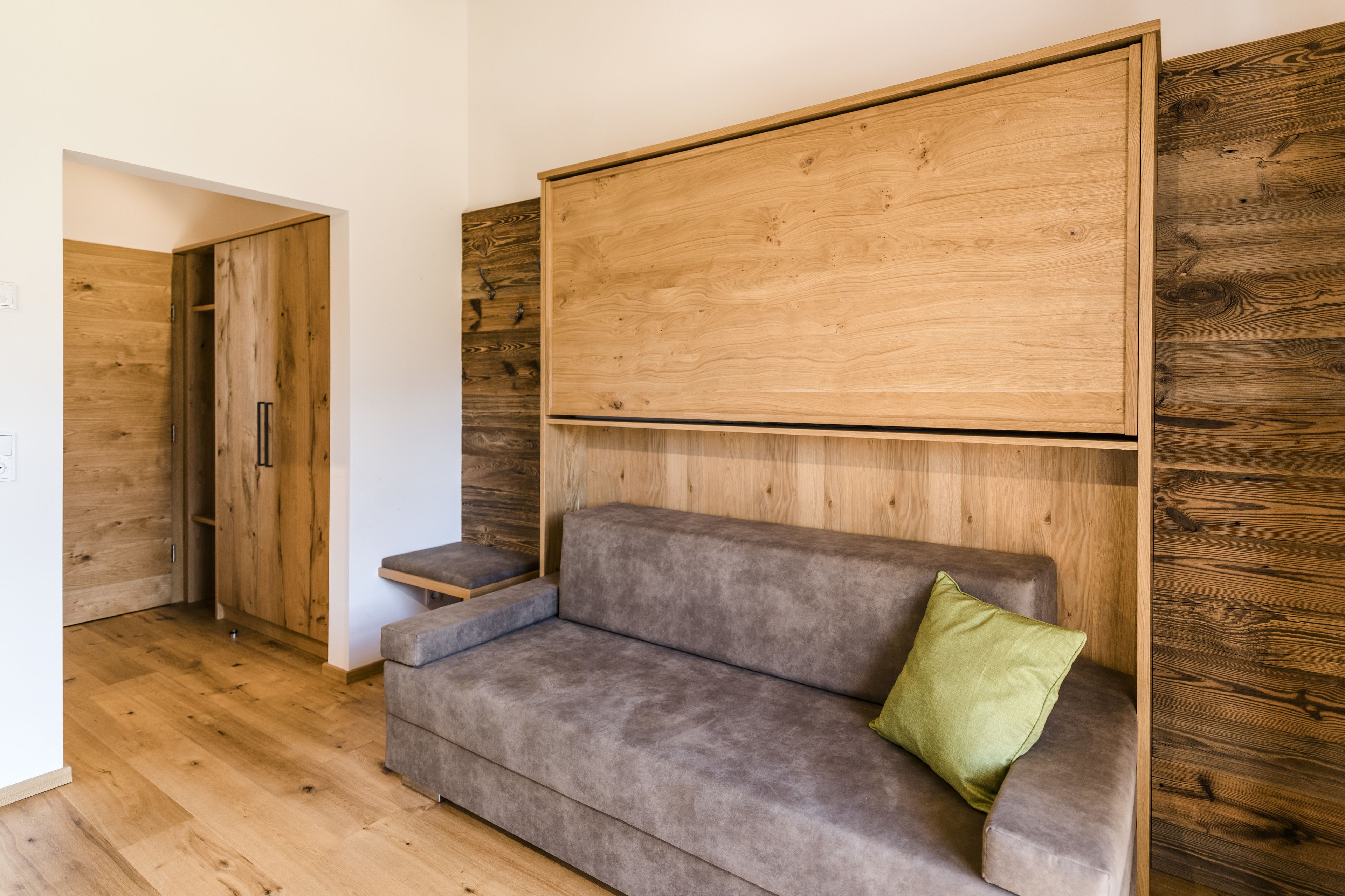 A modern room with a grey sofa, a green pillow, and wooden panel walls.
