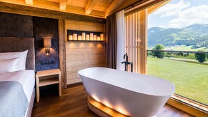 A modern bathroom with a freestanding bathtub, wooden walls, and a large window offering a scenic view of a valley. - Beim Hochfilzer (Soell)