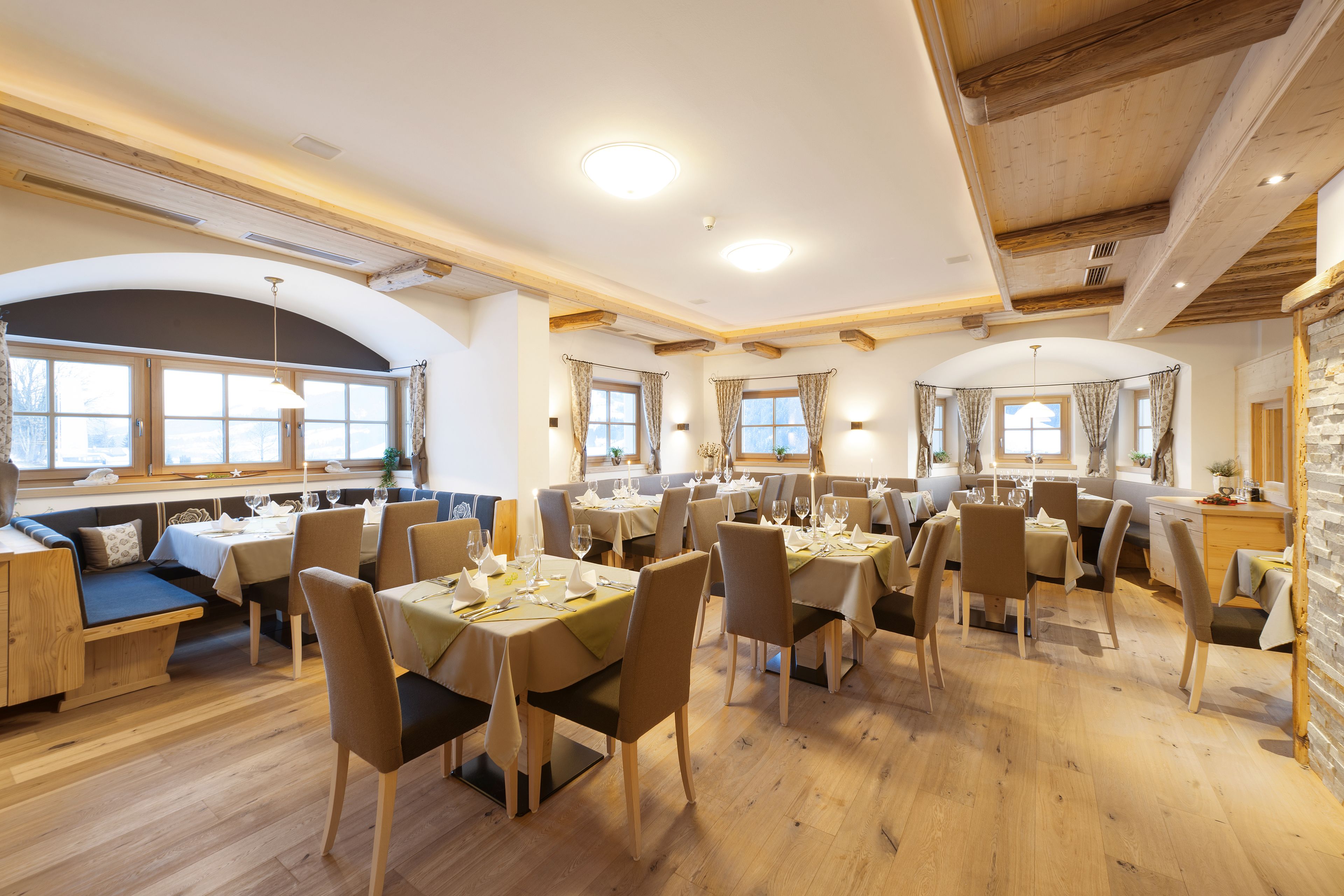 Ein Essbereich mit Holztischen und -stühlen, großen Fenstern mit Vorhängen und einer Steinwand.