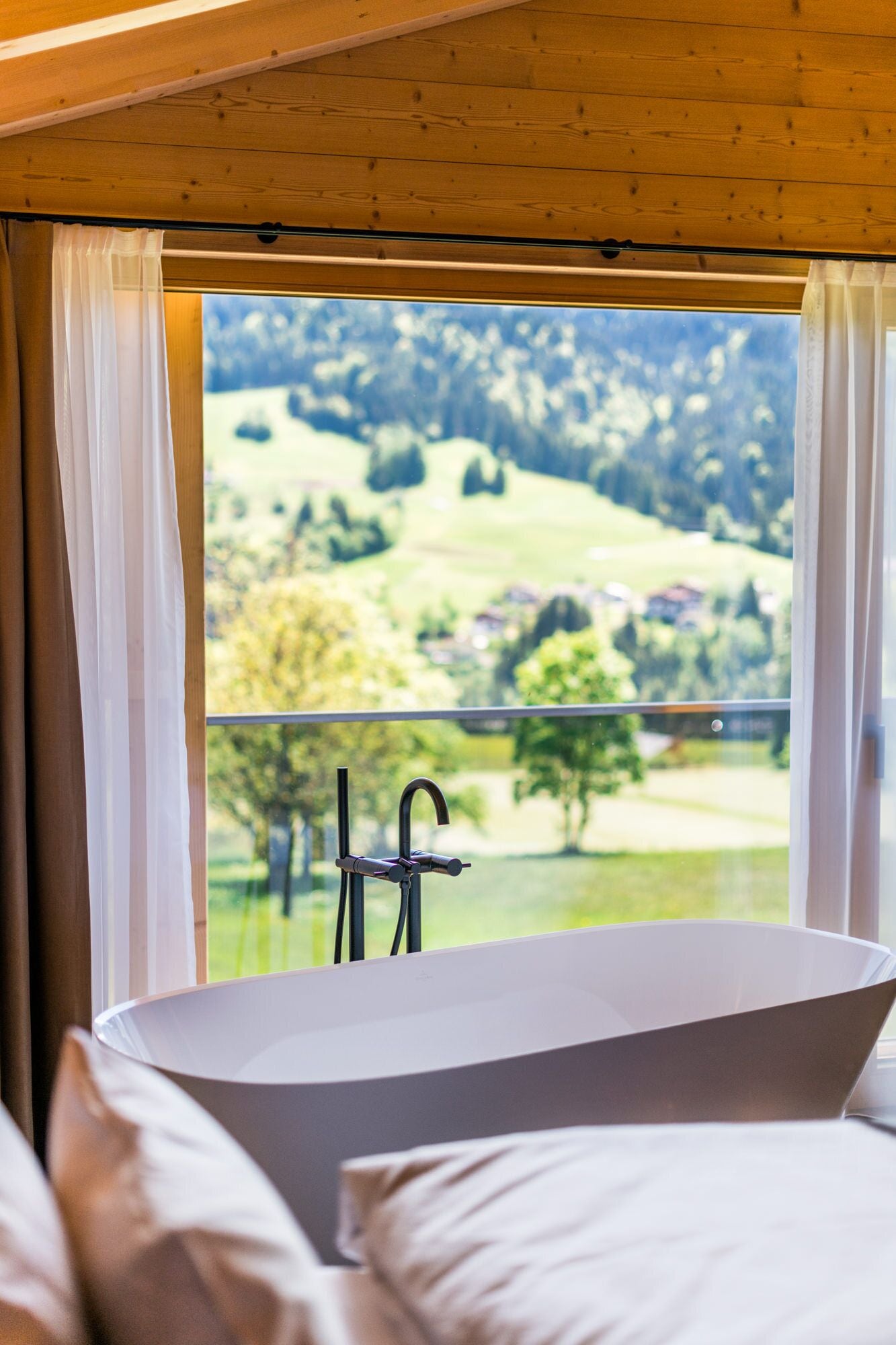 Un baño moderno con una bañera independiente, un ventanal con vistas a un paisaje verde y un techo de madera.