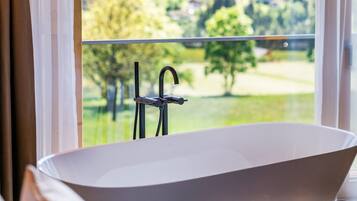 Un baño moderno con una bañera independiente, un ventanal con vistas a un paisaje verde y un techo de madera.