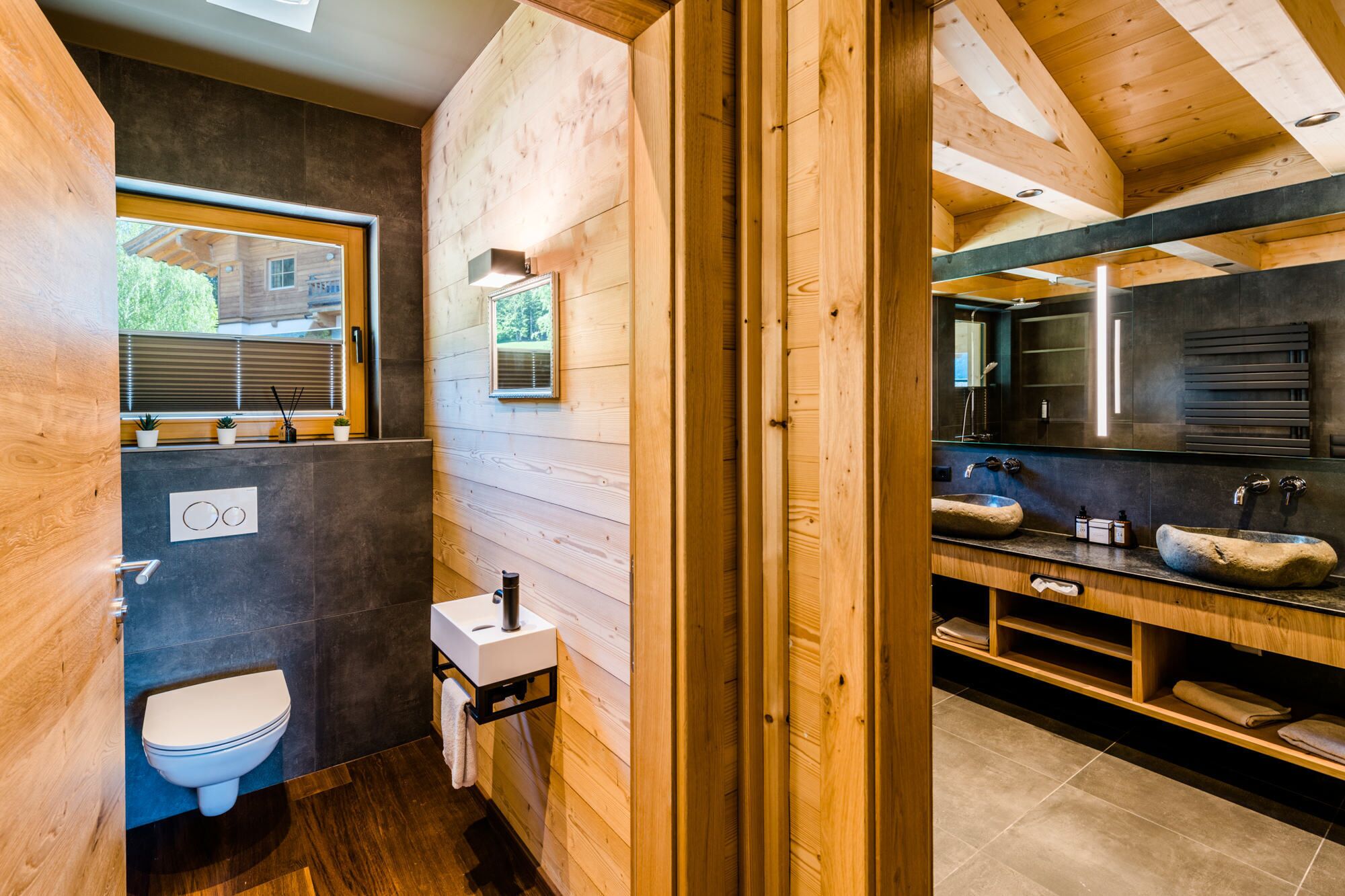 A modern bathroom with wooden walls, a toilet, a sink with a stone basin, and a large mirror above the sink.