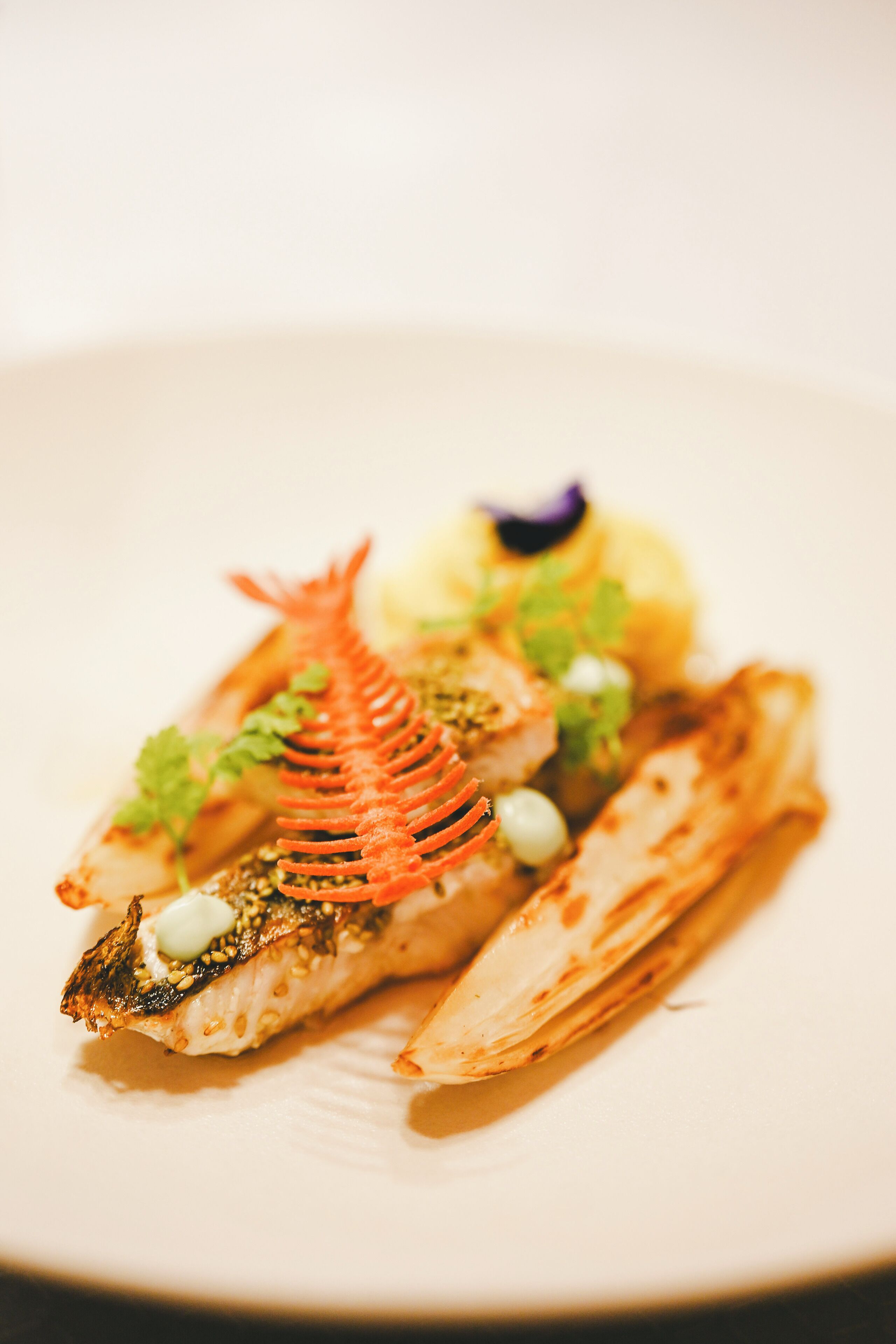 A plate of food with a fish, vegetables, and a decorative element.