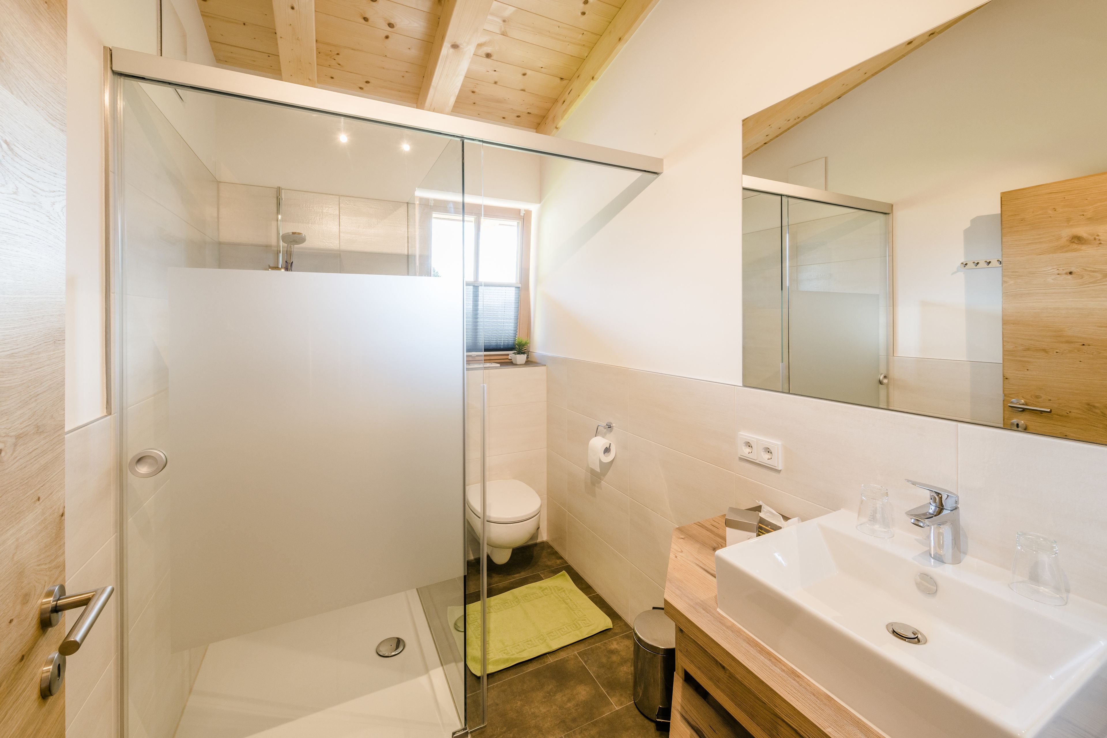 Une salle de bain moderne avec une douche à parois de verre, des toilettes et un lavabo surmonté d’un miroir.