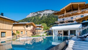 A resort with a swimming pool, wooden buildings, and a mountain backdrop. - Beim Hochfilzer (Soell)