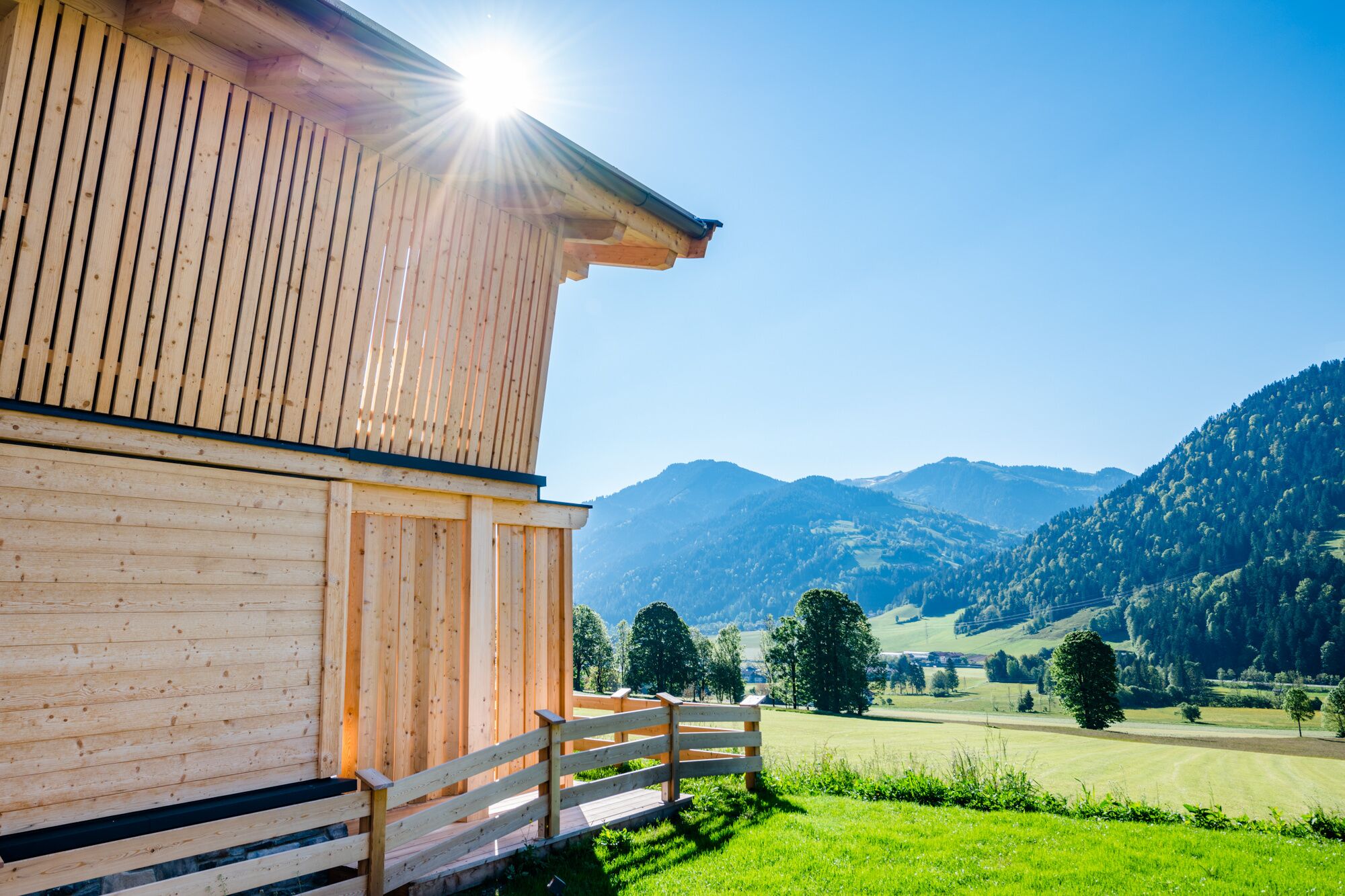 A wooden building with a balcony overlooking a green field and mountains.