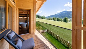 A wooden balcony with a view of a green field and mountains. - Beim Hochfilzer (Soell)