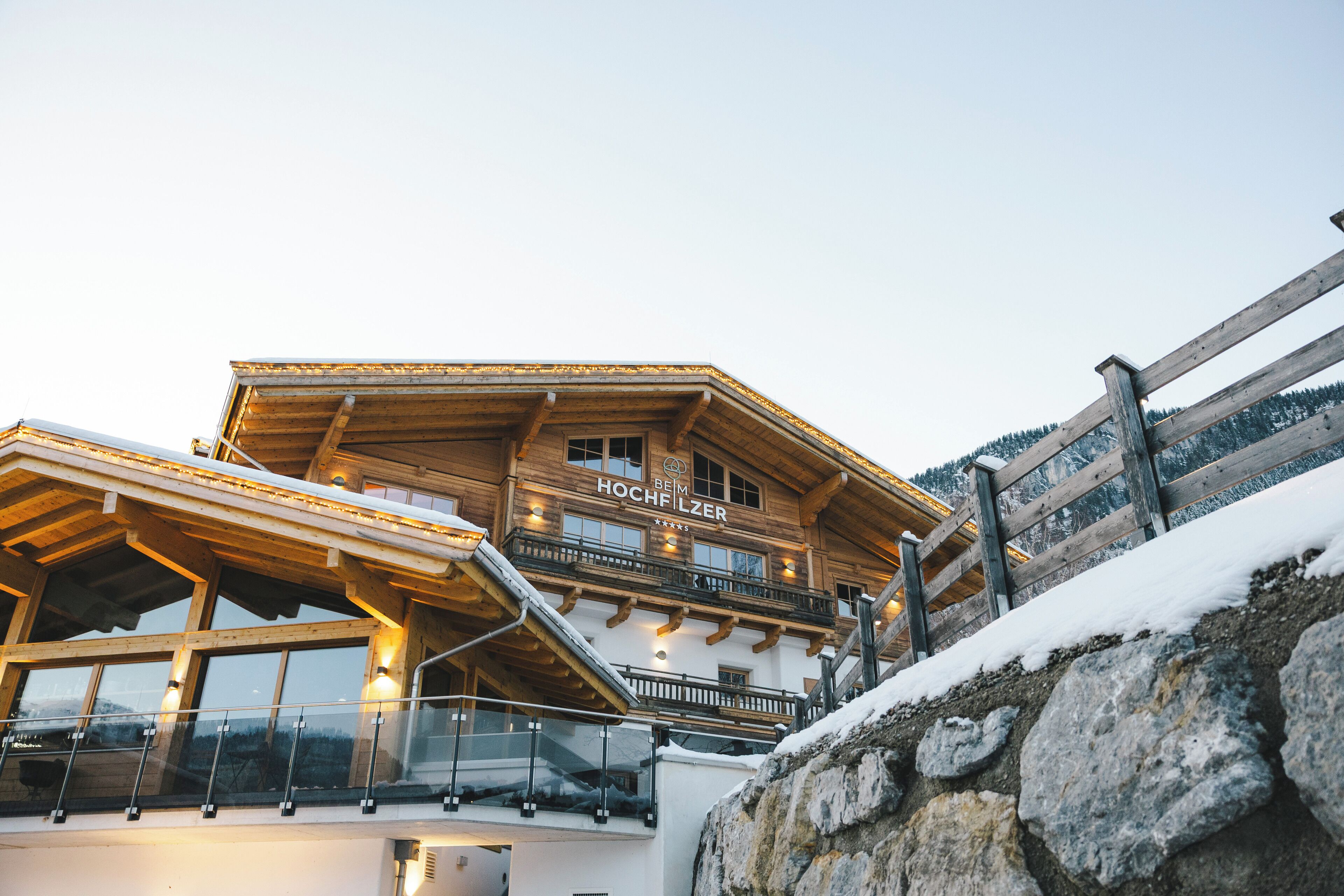 A wooden chalet with a balcony and a sign that reads "BEIM HOCHFILZER."