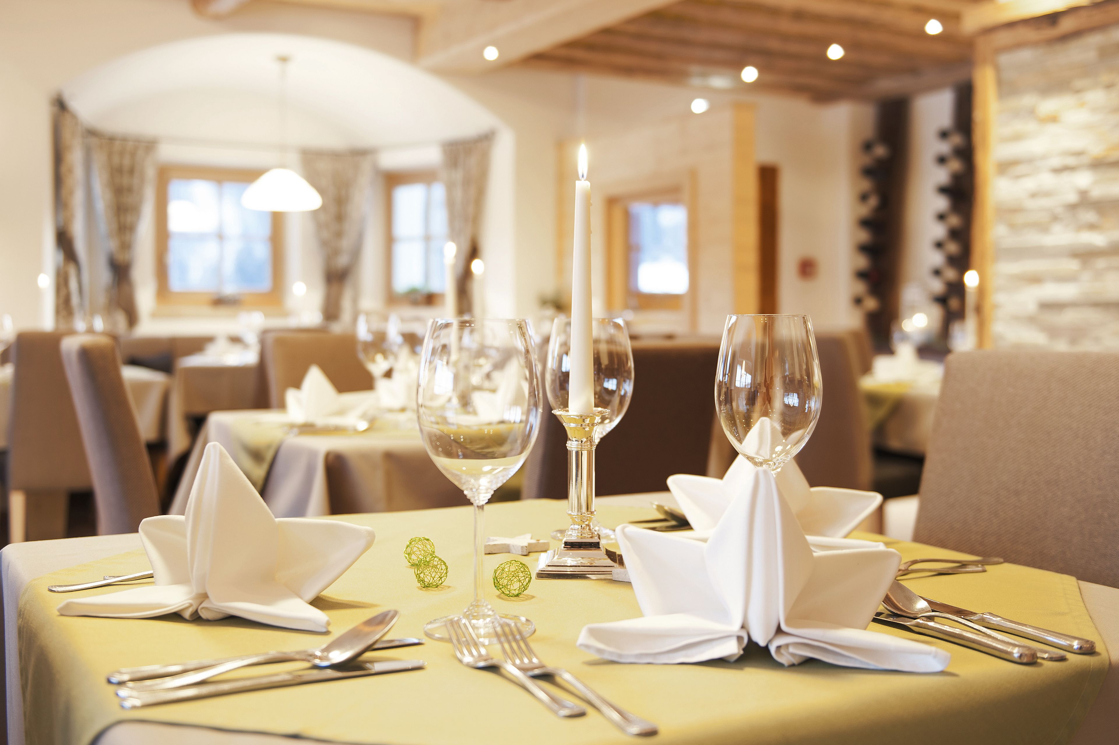 Una mesa de comedor dispuesta con servilletas blancas, cubiertos y copas de vino, con un candelabro encendido como centro de mesa.