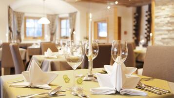 Una mesa de comedor dispuesta con servilletas blancas, cubiertos y copas de vino, con un candelabro encendido como centro de mesa.