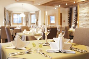 A dining table set with white napkins, silverware, and wine glasses, with a lit candle centerpiece. - Beim Hochfilzer (Soell)