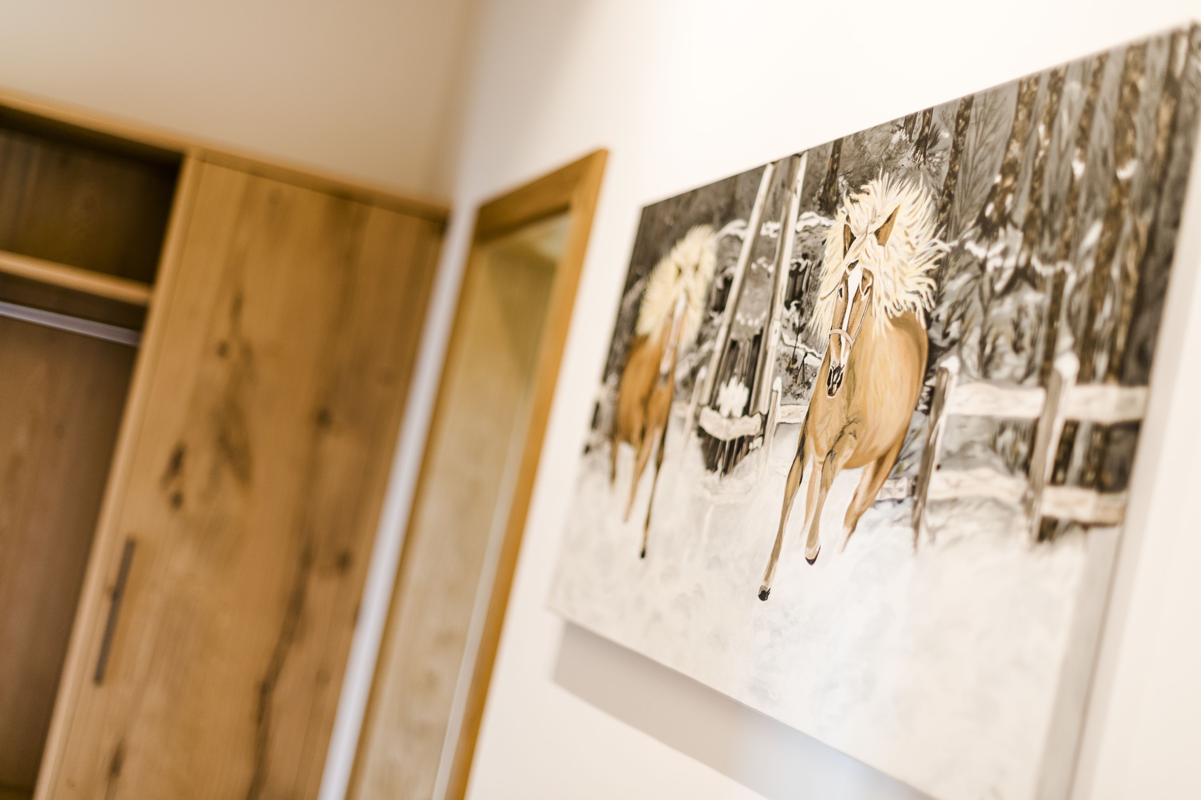 A room with a wooden wardrobe and a painting of horses.