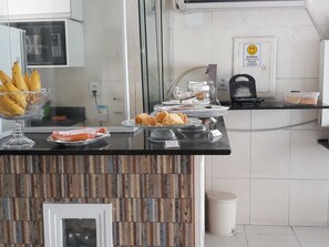 A breakfast bar with various food items, a microwave, and a sign indicating filming. - Pousada Corais da Barra (Salvador)