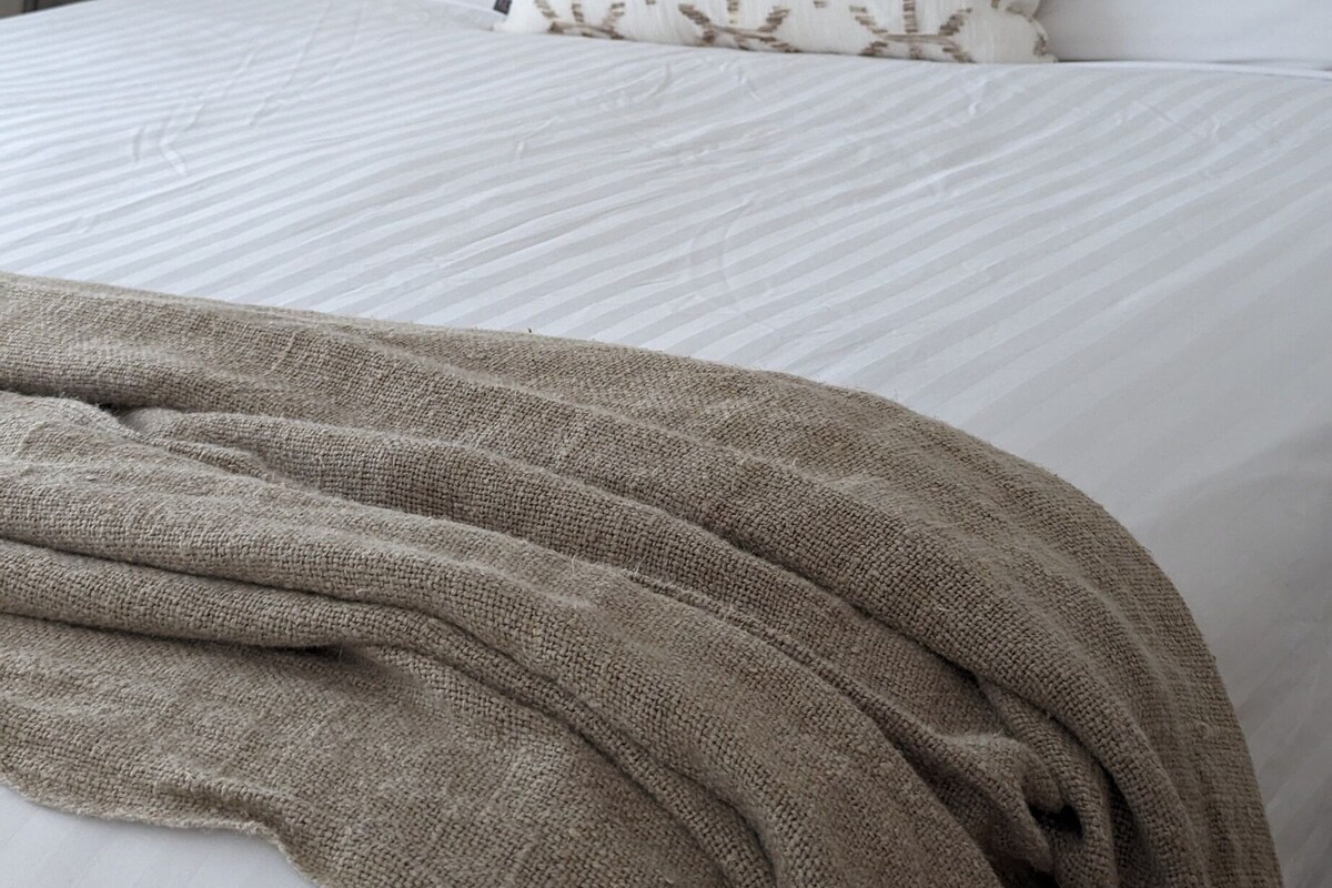 A bed with a wooden headboard, white bedding, and a brown throw blanket.