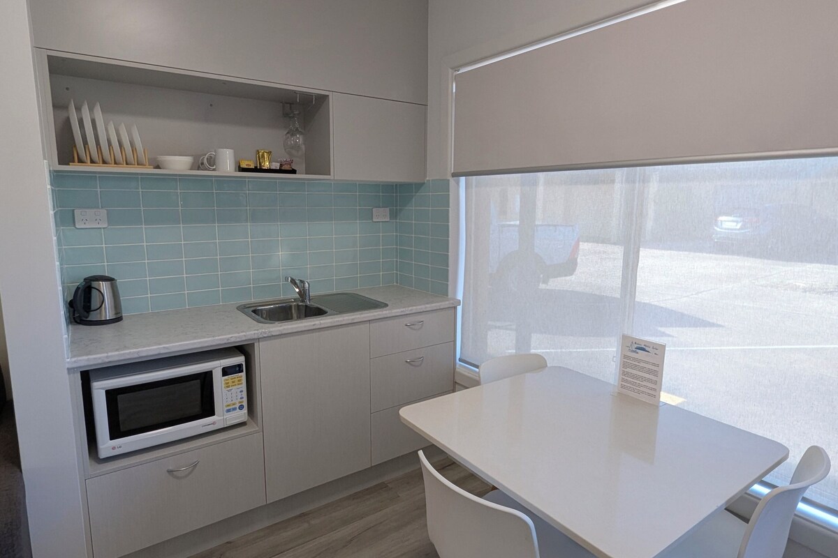 A compact kitchen with a microwave, sink, and a window overlooking a parking area.