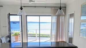 A kitchen with a large island, white cabinetry, pendant lights, and a view of the ocean through a glass door.