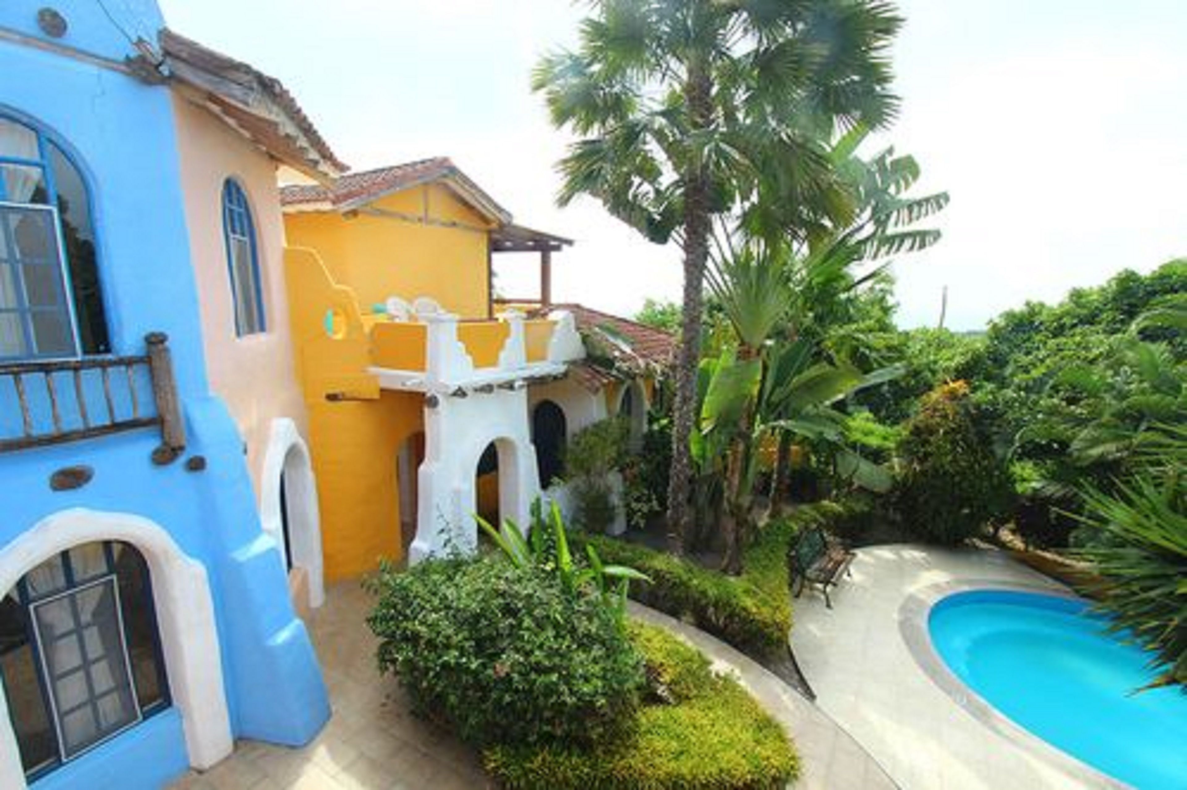 A blue and yellow building with a pool and tropical vegetation.