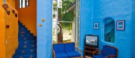 Une pièce avec un mur bleu, un escalier en bois, un canapé bleu, une télévision et un tableau encadré.